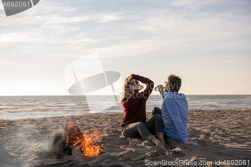 Image of Young Couple Sitting On The Beach beside Campfire drinking beer