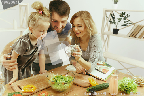 Image of Cute little girl and her beautiful parents are cutting vegetables in kitchen at home