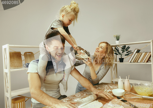 Image of Cute little girl and her beautiful parents preparing the dough for the cake in kitchen at home