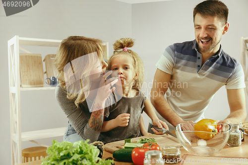 Image of Cute little girl and her beautiful parents are cutting vegetables in kitchen at home