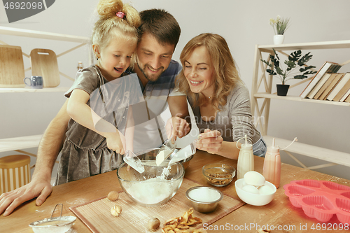 Image of Cute little girl and her beautiful parents preparing the dough for the cake in kitchen at home