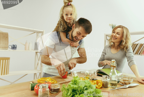 Image of Cute little girl and her beautiful parents are cutting vegetables in kitchen at home