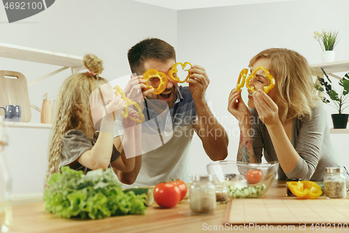 Image of Cute little girl and her beautiful parents are cutting vegetables in kitchen at home