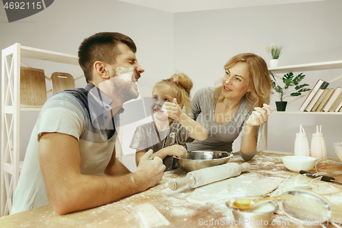 Image of Cute little girl and her beautiful parents preparing the dough for the cake in kitchen at home