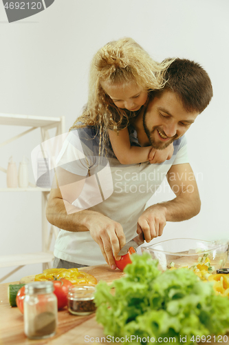 Image of Cute little girl and her beautiful parents are cutting vegetables in kitchen at home