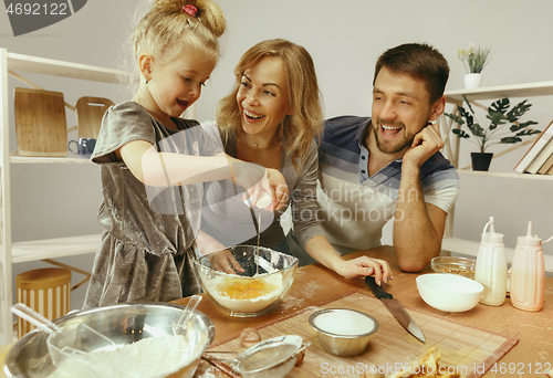 Image of Cute little girl and her beautiful parents preparing the dough for the cake in kitchen at home