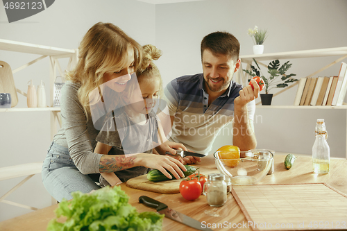 Image of Cute little girl and her beautiful parents are cutting vegetables in kitchen at home