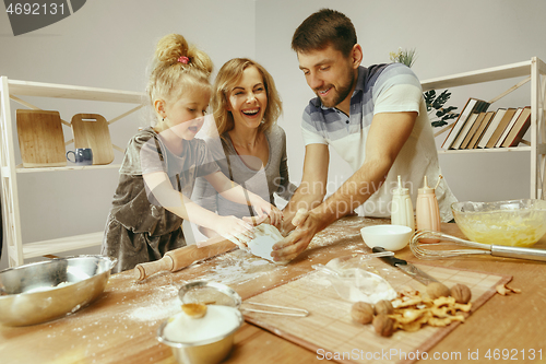 Image of Cute little girl and her beautiful parents preparing the dough for the cake in kitchen at home