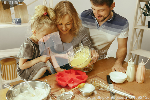 Image of Cute little girl and her beautiful parents preparing the dough for the cake in kitchen at home