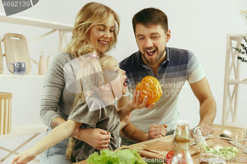 Image of Cute little girl and her beautiful parents are cutting vegetables in kitchen at home