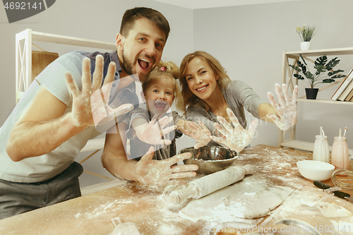 Image of Cute little girl and her beautiful parents preparing the dough for the cake in kitchen at home