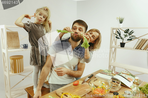 Image of Cute little girl and her beautiful parents are cutting vegetables in kitchen at home