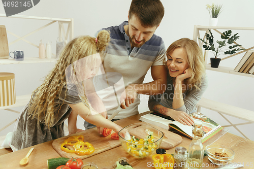 Image of Cute little girl and her beautiful parents are cutting vegetables in kitchen at home