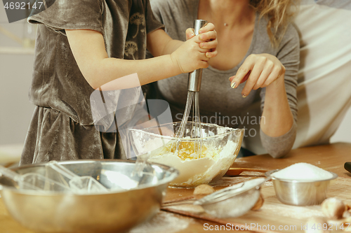 Image of Cute little girl and her beautiful parents preparing the dough for the cake in kitchen at home