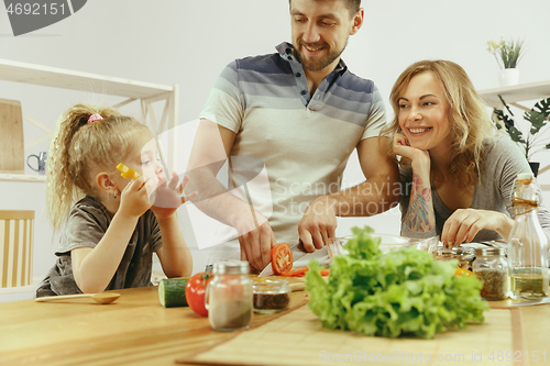 Image of Cute little girl and her beautiful parents are cutting vegetables in kitchen at home