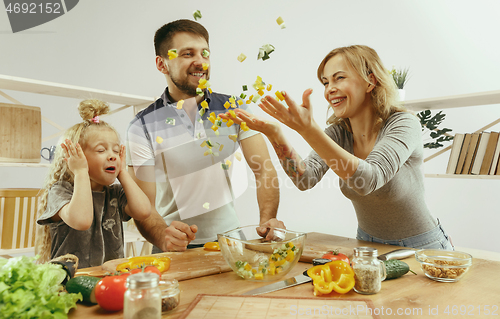 Image of Cute little girl and her beautiful parents are cutting vegetables in kitchen at home