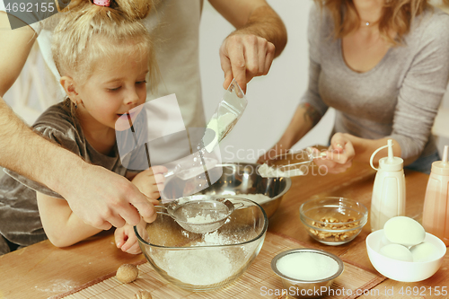 Image of Cute little girl and her beautiful parents preparing the dough for the cake in kitchen at home