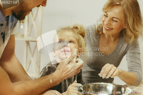 Image of Cute little girl and her beautiful parents preparing the dough for the cake in kitchen at home