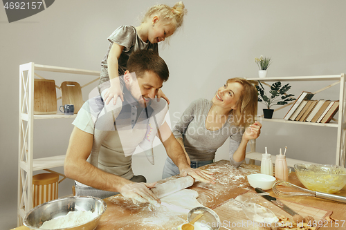 Image of Cute little girl and her beautiful parents preparing the dough for the cake in kitchen at home