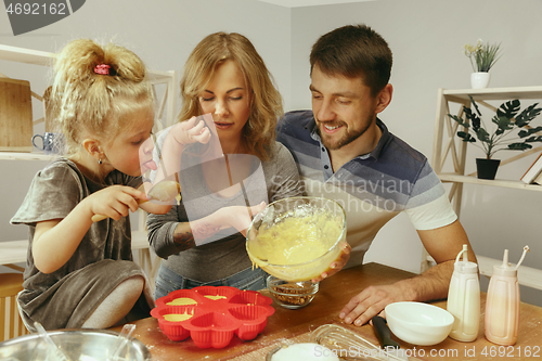 Image of Cute little girl and her beautiful parents preparing the dough for the cake in kitchen at home