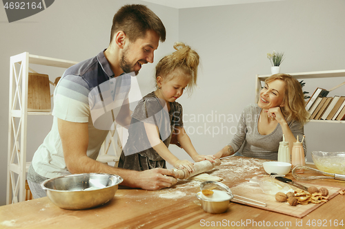 Image of Cute little girl and her beautiful parents preparing the dough for the cake in kitchen at home