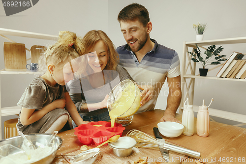 Image of Cute little girl and her beautiful parents preparing the dough for the cake in kitchen at home