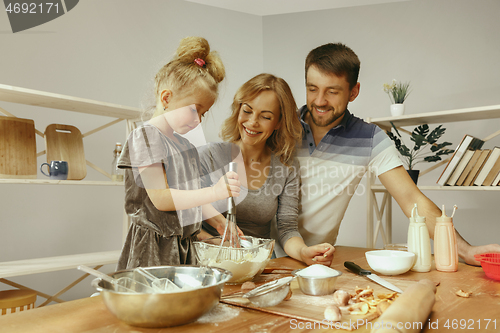 Image of Cute little girl and her beautiful parents preparing the dough for the cake in kitchen at home