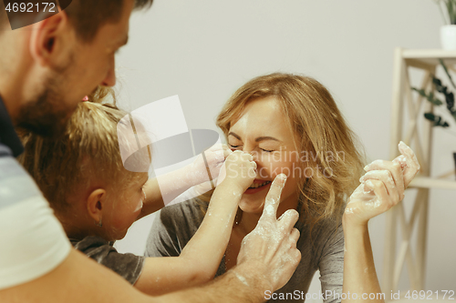 Image of Cute little girl and her beautiful parents preparing the dough for the cake in kitchen at home