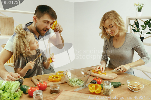 Image of Cute little girl and her beautiful parents are cutting vegetables in kitchen at home