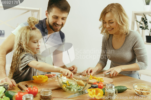 Image of Cute little girl and her beautiful parents are cutting vegetables in kitchen at home