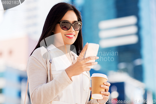 Image of smiling woman with smartphone and coffee in city