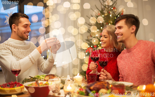 Image of happy friends photographing at christmas dinner