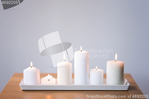 Image of burning white candles on tray on table