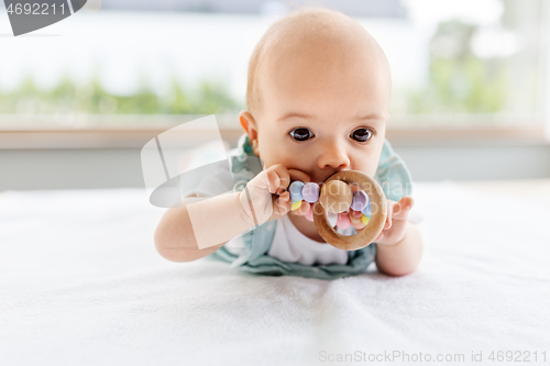 Image of baby girl on white blanket chewing wooden rattle