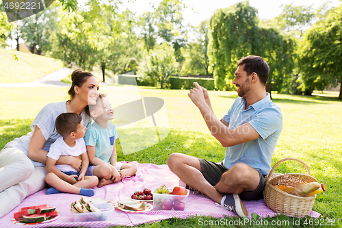 Image of father taking picture of family on picnic at park