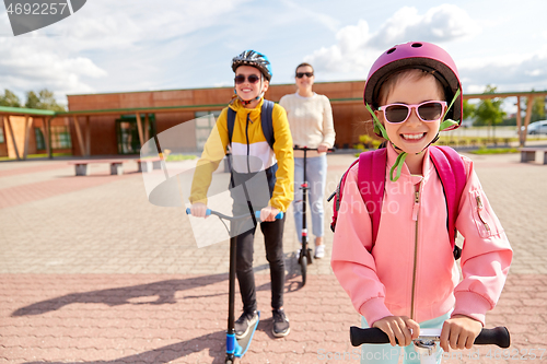 Image of happy school children with mother riding scooters