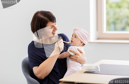 Image of middle-aged mother feeding baby daughter at home