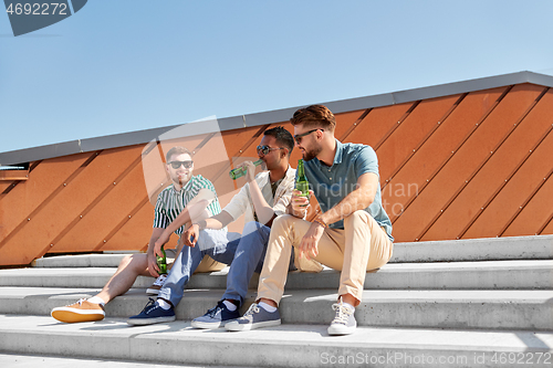 Image of happy male friends drinking beer on street