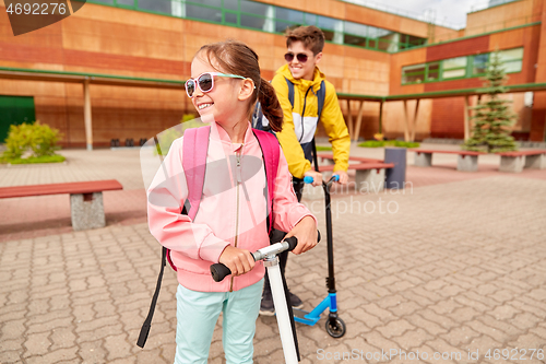 Image of happy school children with backpacks and scooters