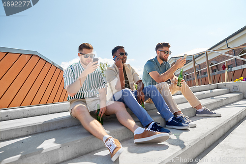 Image of men with smartphones drinking beer on street