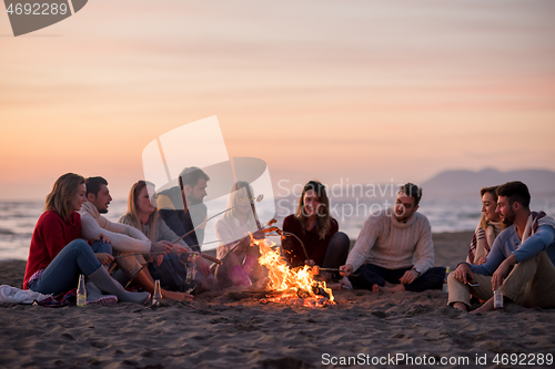 Image of Group Of Young Friends Sitting By The Fire at beach