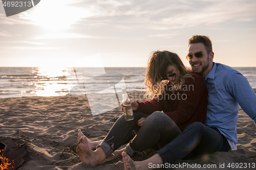 Image of Young Couple Sitting On The Beach beside Campfire drinking beer