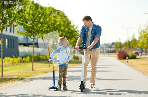 Image of father and little son riding scooters in city