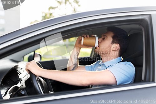 Image of tired man driving car and drinking coffee