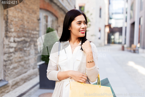 Image of asian woman with shopping bags walking in city