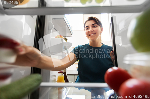 Image of happy woman taking food from fridge at home