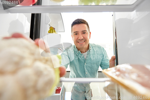 Image of man taking vegetable from fridge at home kitchen