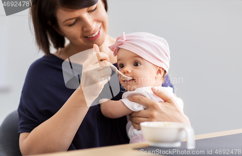 Image of middle-aged mother feeding baby daughter at home