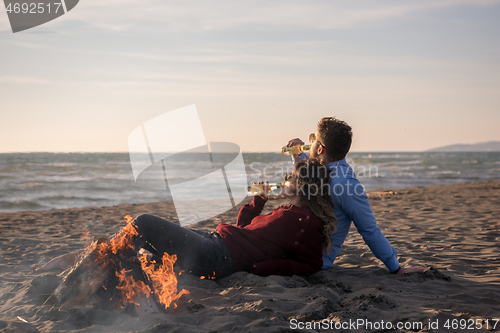 Image of Young Couple Sitting On The Beach beside Campfire drinking beer