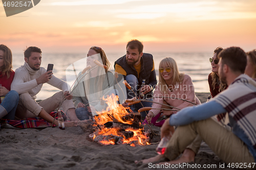 Image of Group Of Young Friends Sitting By The Fire at beach